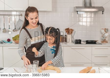 Happy Asian Mother and Daugther is breaking egg to make Bakery in kitchen together, for family fun a