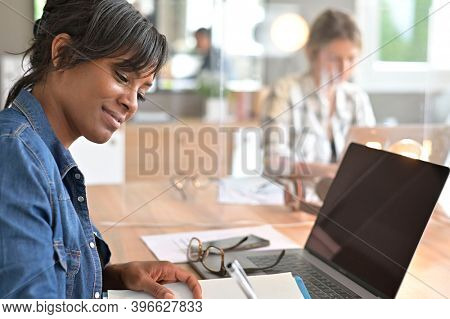 Office worker woman in open space area, protected by plexiglas
