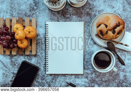 Notebook On The Table, There Is Breakfast Placed On The Side, Top View.
