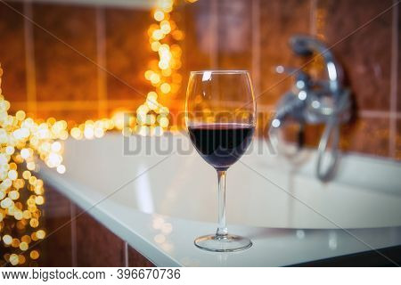 Close Up Of Wine Glass With Red Wine Near Bathtub With Lights On The Background, Relaxtion And Spa C