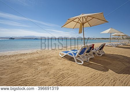 Landscape View Across An Empty Sandy Tropical Beach Resort Shoreline With Sun Loungers To The Open O