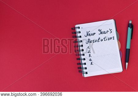 Writing In A Notebook New Years Resolutions On Red Background. New Years Resolutions Concept. Flat L
