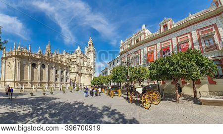 Seville, Spain - October 18. 2020: Horse Drawn Carriages At Plaza Triunfo With Tourists At The Back 