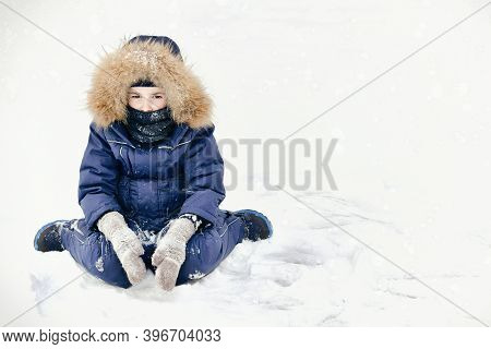 A Frustrated Child With Sad Eyes In A Jumpsuit With A Fur Hood And Ruddy Cheeks From Frost. Sits On 
