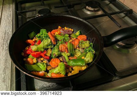 Lots Of Colorful Vegetables Are Fried In A Frying Pan On The Kitchen Stove. Carrots, Capsicum, Peppe