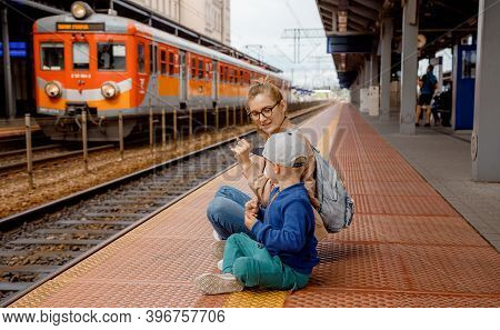 Woman With Son On The Platform Near The Train. Girl With A Preschool Boy Sitting At The Train Statio