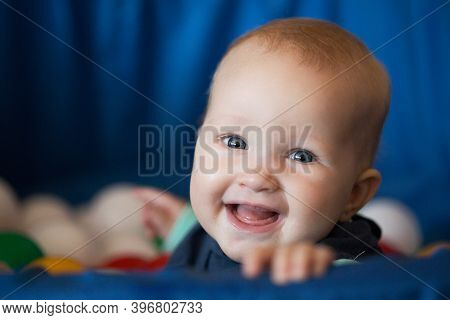 Cheerful Smiling Baby Girl With Blond Hair And Blue Eyes Sitting In The Ball Pit. Bright Colors Port