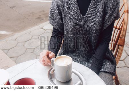 Woman In A Cozy Gray-blue Vest Spends Time Outdoors In The City. Female Sits In Street Cafe On A Woo
