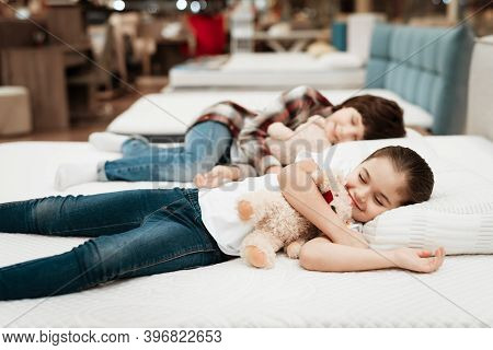 Little Happy Girl Hugs Bear Lying On Bed. In Background Little Boy Sleeps.