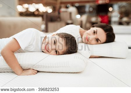 Smiling Little Girl With Beautiful Mother Hugs Pillows In Store Of Orthopedic Mattresses.