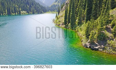 Kolsay Lake Among Green Hills And Mountains. The Mountain Lake Is Surrounded By Green Forest, Tall C