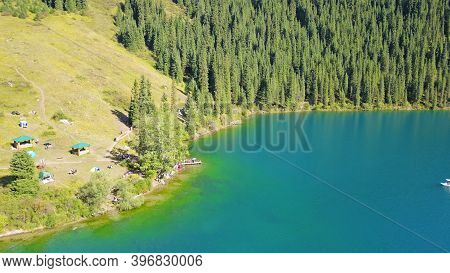 Kolsay Lake Among Green Hills And Mountains. The Mountain Lake Is Surrounded By Green Forest, Tall C