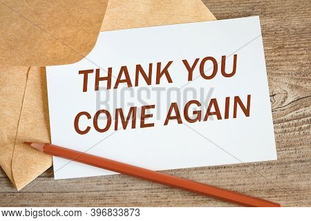 Open Craft Envelope And Card With The Words Thank You Come Again, Pencil On A Wooden Surface.