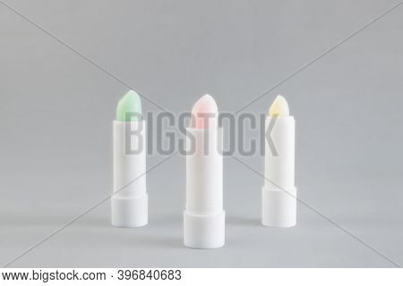 White Tube Of Pink, Green And Yellow Lip Balm To Protect And Nourish Lips On A Gray Background. Wint