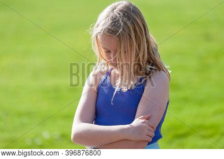 Moody Young Blonde Girl With Arms Folded Sulks In A Field.