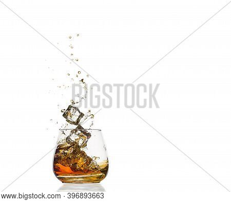 A Glass Of Cognac With Splashes From The Ice Cube Isolated On White. Alcohol Splashes. Whisky Or Cog