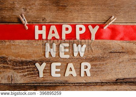 Happy New Year Inscription In Wooden Letters On A Wooden Background. The Word Happy On The Red Ribbo