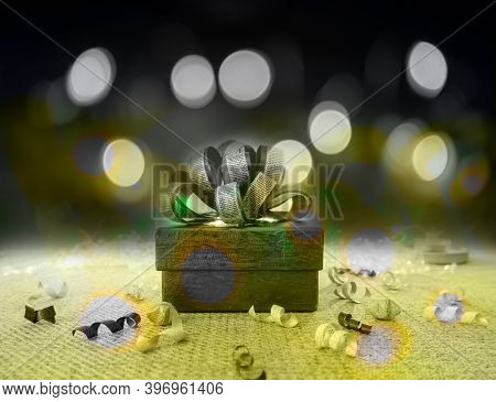 A Grey Gift Box With Gray Ribbon On Green Fabric Under Bokeh Yellow Lighting On Dark Background