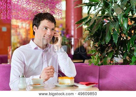 Young man in a cafe or ice cream parlor eating a cake and using his phone, maybe he is single or waiting for someone