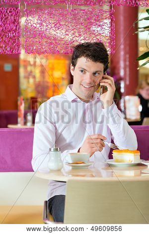 Young man in a cafe or ice cream parlor eating a cake and using his phone, maybe he is single or waiting for someone