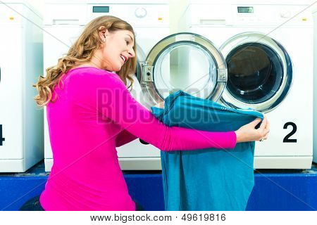 Woman in a launderette, washing her dirty laundry, in the background are washing machines, a female student is pleased about her clean blouse