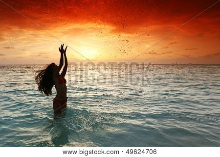 Cheerful pretty young woman splashin in sea on sunset