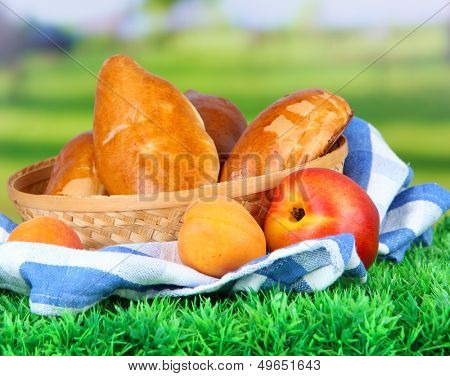 Fresh baked pasties with fruits, in wicker basket, on grass, on bright background