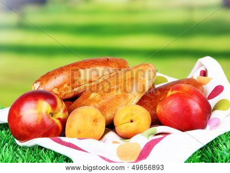Fresh baked pasties with fruits, on color napkin, on grass, on bright background