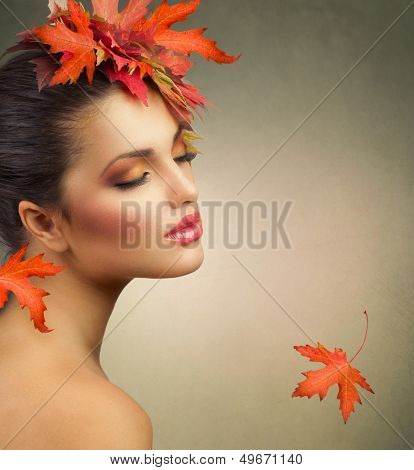 Autumn Woman Fashion Portrait. Beauty Autumn Girl with colorful yellow and red Leaves on her Head. Hairstyle and Makeup. Fall. Fashion Model closeup