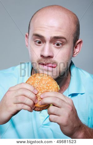 Funny man eating hamburger on grey background