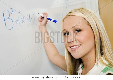 Closeup portrait of beautiful student solving algebra equation on whiteboard in classroom