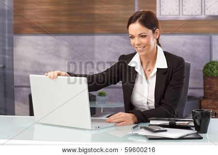 Happy businesswoman sitting at desk shutting down laptop computer, finishing work.