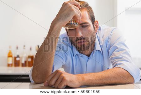 Drunk businessman clutching whiskey glass to head at the local bar