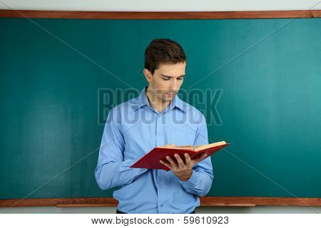 Young teacher with book near chalkboard in school classroom