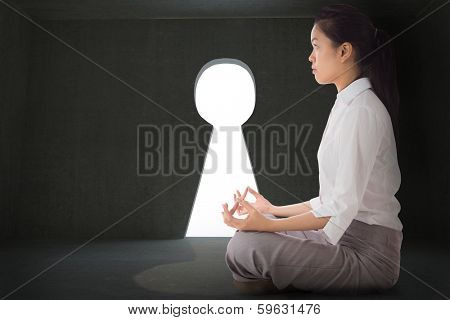Businesswoman sitting in lotus pose against grey room with keyhole door