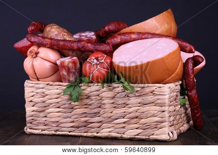 Lot of different sausages in basket on wooden table on black background