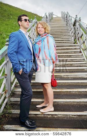 Happy pregnant woman in white and stylish man stand on stairs outdoor.