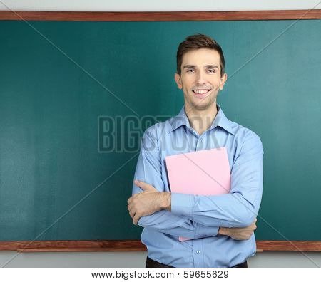 Young teacher with book near chalkboard in school classroom
