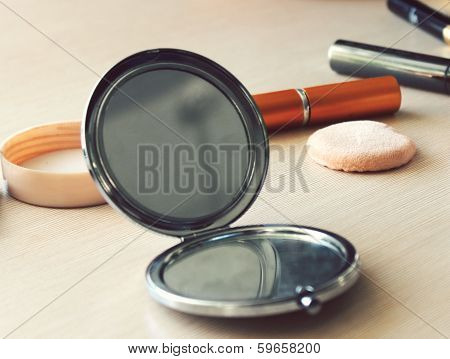 Compact pocket mirror next to powder and a powder puff and other cosmetics