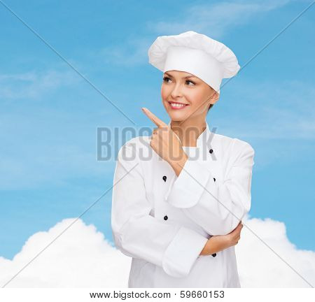 cooking, advertisement and food concept - smiling female chef, cook or baker pointing finger to something