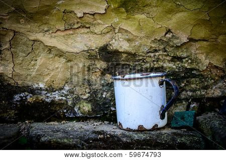Old enamelware mug against a grungy wall