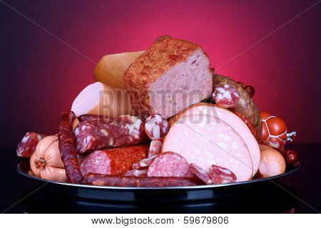 Lot of different sausages on salver on dark colorful background