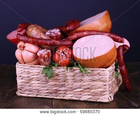 Lot of different sausages in basket on wooden table on black background