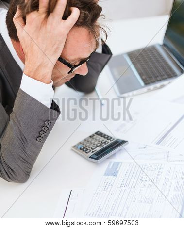 tax, business and stress concept - stressed businessman with papres, laptop and calculator