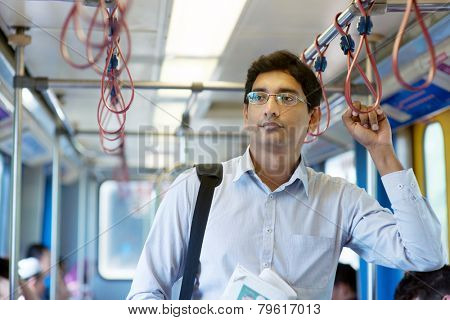 Asian Indian businessman taking ride to work, standing inside train.