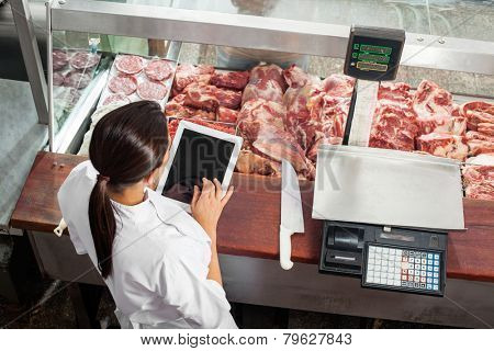 High angle rear view of female butcher using digital tablet at display counter in butchery