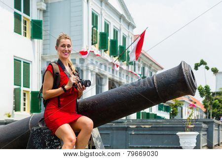 Woman tourist  sitting on cannon in old Batavia colonial district of Jakarta, Indonesia
