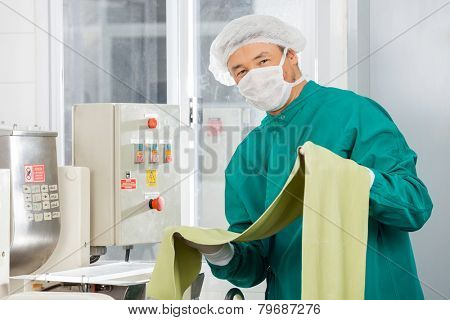 Portrait of chef in protective workwear holding green spaghetti pasta sheet by machine at commercial kitchen