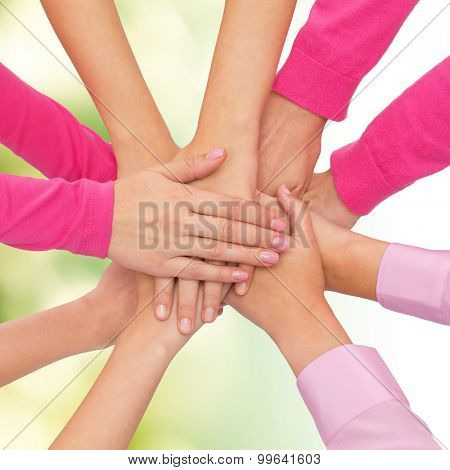 feminism, women power and breast cancer awareness concept - close up of women hands on top of each other over white background