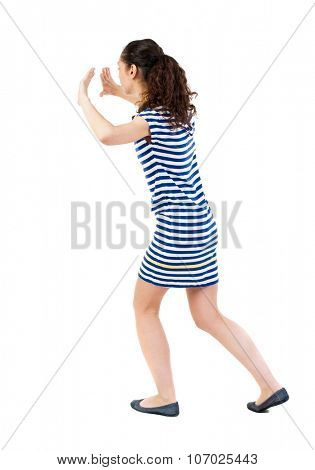 back view of woman pushes wall. Isolated over white background. Rear view people collection. backside view of person. African-American woman in a striped dress in barely pushes something on my own.